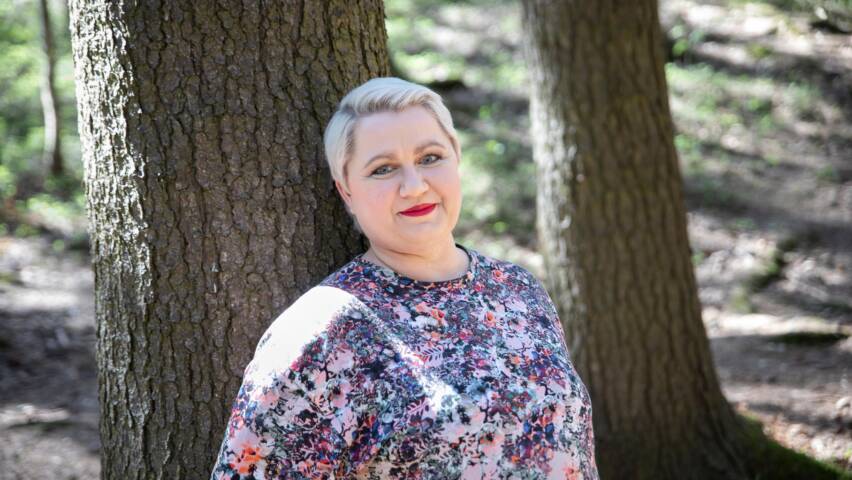 Kuvassa vaalea lyhythiukisnen nainen nojaa puunrunkoon